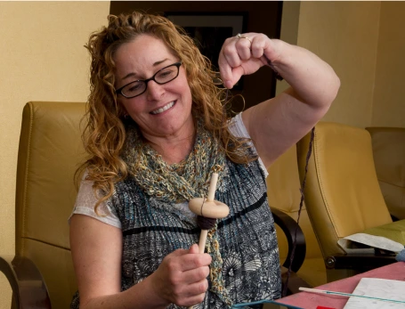 A woman spinning yarn and smiling